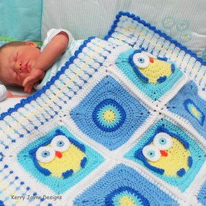 May include: A blue and white crocheted baby blanket with a yellow owl design. The blanket is made with a variety of stitches and has a scalloped edge. The blanket is lying on a white crib mattress with a baby sleeping on it.