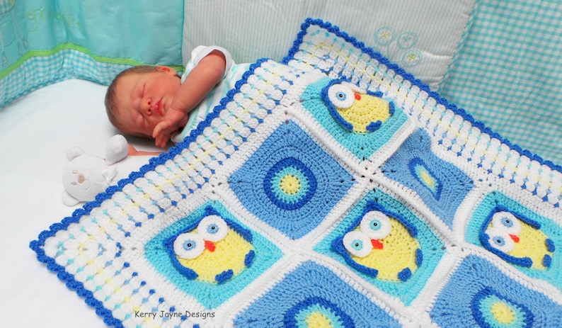 May include: A blue and white crocheted baby blanket with a yellow owl design. The blanket is made with a variety of stitches and has a scalloped edge. The blanket is lying on a white crib mattress with a baby sleeping on it.