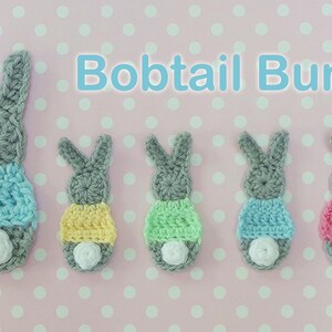 May include: Crocheted gray bunny figures with colorful skirts and white bobtails. The image features the text "Bobtail Bunnies" and "Kerry Jayne Designs Pattern". The bunnies are arranged on a pink polka dot background.