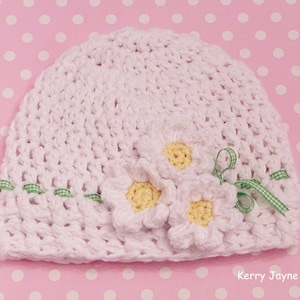 May include: White crocheted baby hat with three white crocheted flowers and green ribbon accents. Kerry Jayne Designs.