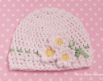 Peut inclure: Chapeau de bébé en crochet blanc avec trois fleurs en crochet blanc et des accents de ruban vert. Kerry Jayne Designs.