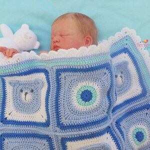K&ouml;nnte beinhalten: Eine blaue und wei&szlig;e geh&auml;kelte Babydecke mit einem B&auml;renmuster. Die Decke hat einen wei&szlig;en geh&auml;kelten Rand mit einem gewellten Saum. Ein wei&szlig;er Teddyb&auml;r liegt auf der Decke neben einem Baby.