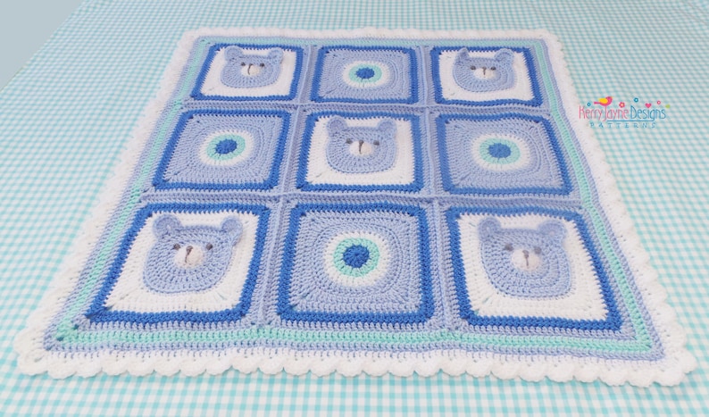 K&ouml;nnte beinhalten: Eine blaue und wei&szlig;e geh&auml;kelte Babydecke mit einem gewellten Rand. Die Decke besteht aus Quadraten mit B&auml;renk&ouml;pfen und Kreisen in der Mitte. Die Decke liegt auf einer blau-wei&szlig; karierten Oberfl&auml;che.