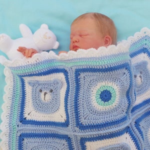 K&ouml;nnte beinhalten: Ein Baby schl&auml;ft auf einer blauen und wei&szlig;en geh&auml;kelten Babydecke mit einem wei&szlig;en Teddyb&auml;ren. Die Decke hat einen gewellten Rand und zeigt einen blauen B&auml;ren und ein blaues Kreisdesign.