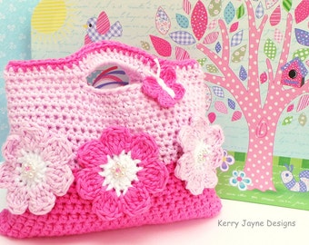 Könnte beinhalten: Eine rosa und weiße gehäkelte Tragetasche mit Schmetterlings- und Blumenverzierungen. Die Tasche hat einen Henkel und ist mit einem strukturierten Stich gearbeitet. Die Tasche steht auf einem Tisch mit rosa und grünem Hintergrund.
