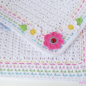 May include: White crochet baby blanket with a colorful border and flower appliques. The blanket has a pink flower with a ladybug in the center, and two white daisies with yellow centers. The border is made of multiple rows of different colored yarn.