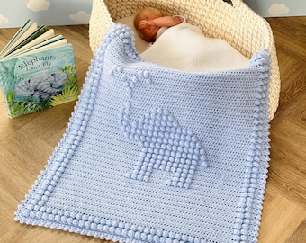 May include: A light blue crocheted baby blanket with a textured elephant design. The blanket has a white border with small pom-poms around the edges.