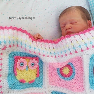 May include: A pink, white, and blue crocheted baby blanket with an owl design. The blanket has a scalloped edge and is made with a variety of stitches. The blanket is shown with a baby doll sleeping on it.