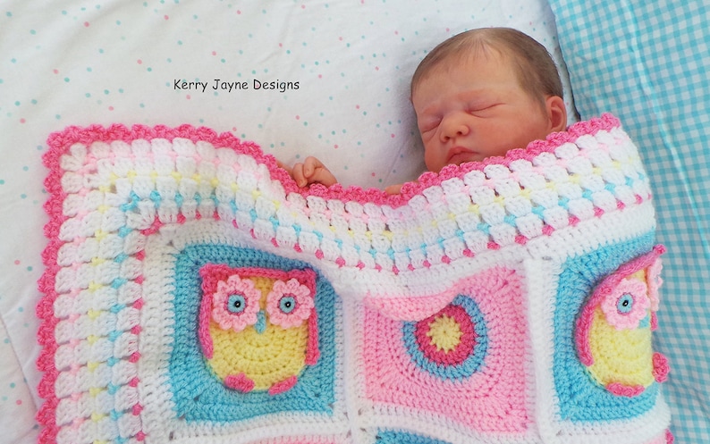 May include: A pink, white, and blue crocheted baby blanket with an owl design. The blanket has a scalloped edge and is made with a variety of stitches. The blanket is shown with a baby doll sleeping on it.