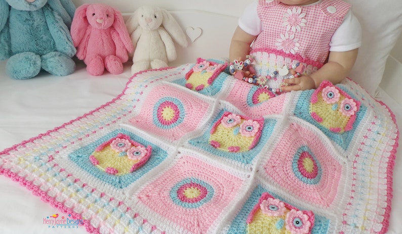 May include: A pink, blue, and white crocheted baby blanket with a pattern of owls. The blanket is made with soft yarn and has a delicate crocheted border.