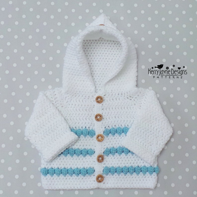 May include: White crocheted hooded cardigan with blue and white stripes and wooden buttons. The cardigan has a hood and long sleeves.