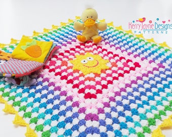 May include: A rainbow crochet baby blanket with a yellow sun applique in the center. The blanket has a white border and a yellow scalloped edge. A yellow duck toy and a multi-colored book are on the blanket. The text "Kerry Jayne Designs PATTERNS" is in the top right corner of the image.