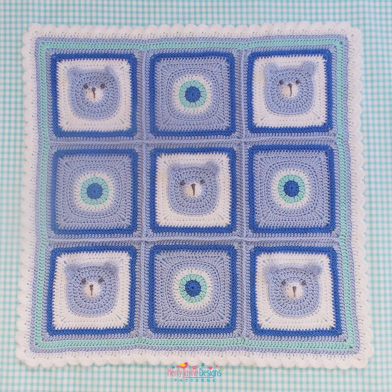 K&ouml;nnte beinhalten: Eine blaue und wei&szlig;e geh&auml;kelte Babydecke mit einem sich wiederholenden Muster aus B&auml;ren und Kreisen. Die Decke hat einen wei&szlig;en geh&auml;kelten Rand mit einem hellblauen und gr&uuml;nen Besatz.