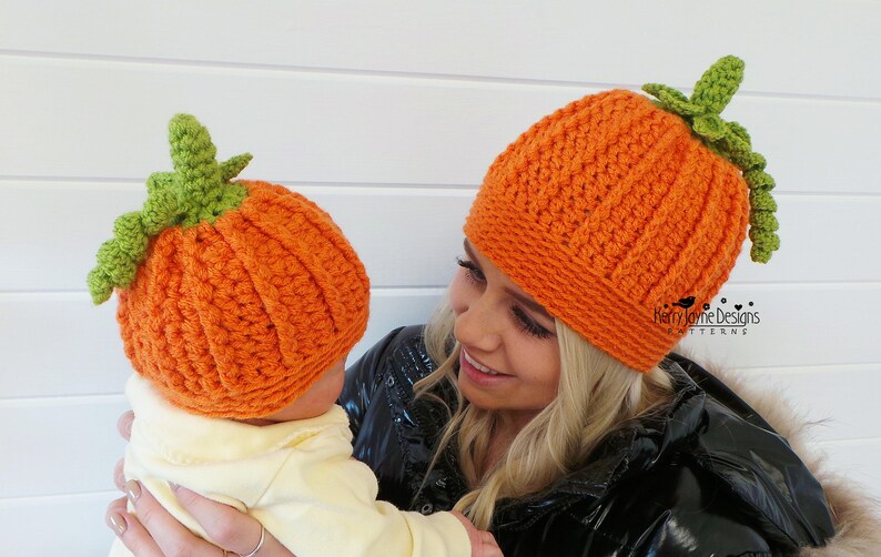 May include: A woman and a baby wearing matching orange and green crocheted pumpkin hats. The hats have a textured stitch pattern and a green stem on top.