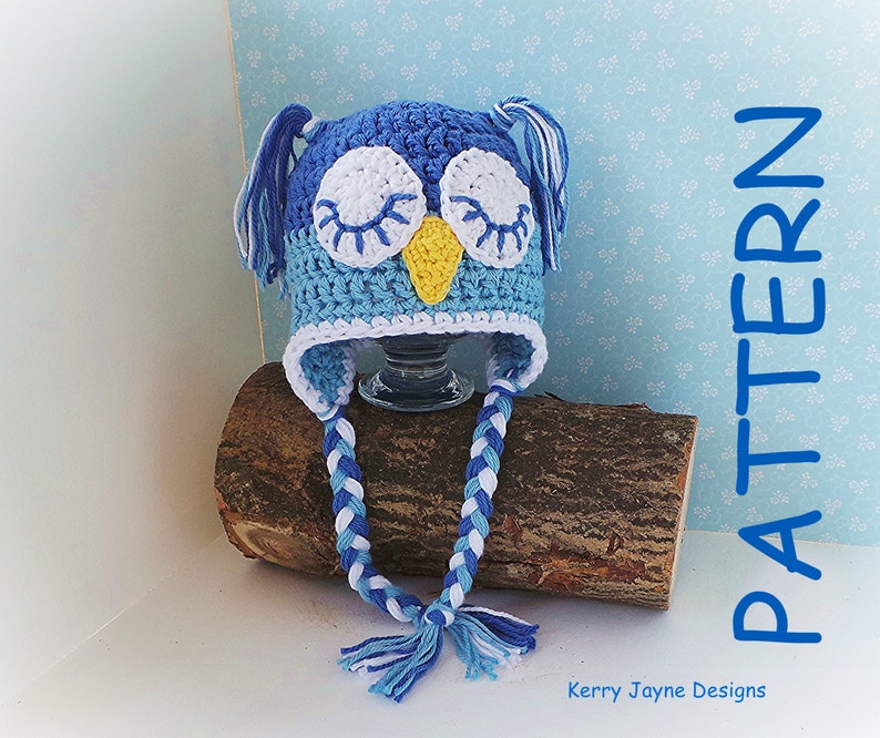 May include: Blue and white crocheted owl hat with long braided ties. The hat has a yellow beak and white eyes. The hat is sitting on a piece of wood. "PATTERN" is written vertically in blue on the right side of the image. "Kerry Jayne Designs" is written in black at the bottom of the image.
