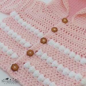 May include: A pink crocheted baby cardigan with white bobbles and wooden flower buttons.