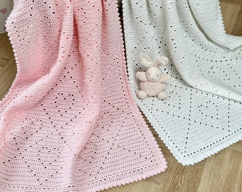 May include: Two crocheted baby blankets, one pink and one white, with a delicate stitch pattern. The blankets are laid out on a wooden floor with a small stuffed bunny on top of the white blanket.