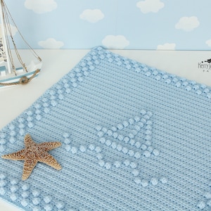May include: A light blue crocheted baby blanket with a sailboat design made with raised stitches. The blanket is decorated with a starfish and has a white border.