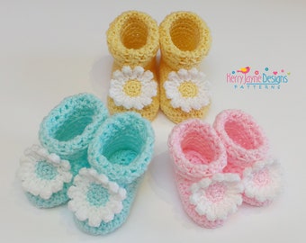 Puede incluir: Tres pares de botines de bebé tejidos a crochet con adornos de flores de margarita. Los botines son de color amarillo, azul y rosa.