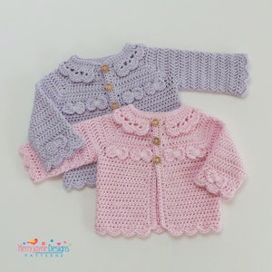 May include: Two crocheted baby cardigans with scalloped edges and button closures. One cardigan is lavender and the other is pink.
