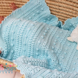 May include: A light blue crocheted baby blanket with a scalloped edge and a textured bobble stitch pattern. The blanket is in a wicker basket with a baby and a white stuffed lamb.