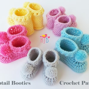 Puede incluir: Seis pares de botines de beb&eacute; tejidos a crochet en varios colores, incluyendo rosa, azul, amarillo y gris. Cada bot&iacute;n tiene un peque&ntilde;o pomp&oacute;n en la parte superior. Los botines est&aacute;n dispuestos en un c&iacute;rculo sobre un fondo blanco. Bobtail Booties Crochet Pattern.