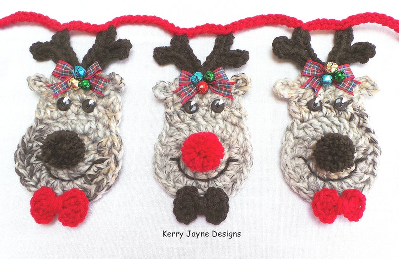 Puede incluir: Una guirnalda de tres cabezas de reno de crochet con lazos rojos y negros, cuernos marrones y narices de pomp&oacute;n. Los renos est&aacute;n unidos con una cuerda roja de crochet. El texto "Kerry Jayne Designs" es visible en la parte inferior de la imagen.