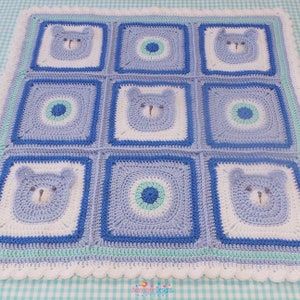 K&ouml;nnte beinhalten: Eine blaue und wei&szlig;e geh&auml;kelte Babydecke mit einem sich wiederholenden Muster aus B&auml;renk&ouml;pfen und Kreisen. Die Decke hat einen wei&szlig;en geh&auml;kelten Rand mit einem gewellten Saum.
