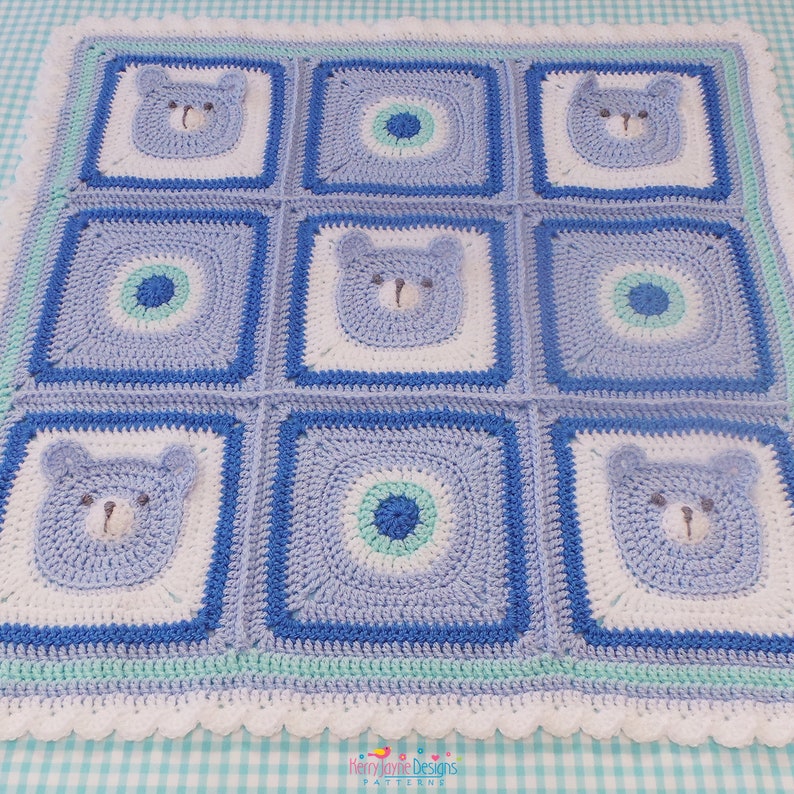 K&ouml;nnte beinhalten: Eine blaue und wei&szlig;e geh&auml;kelte Babydecke mit einem sich wiederholenden Muster aus B&auml;renk&ouml;pfen und Kreisen. Die Decke hat einen wei&szlig;en geh&auml;kelten Rand mit einem gewellten Saum.