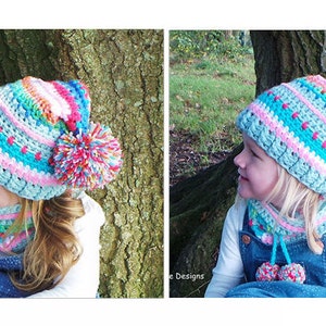 May include: Two children wearing matching crocheted hats and neck warmers. The hats are blue, pink, and white with colorful pom-poms. The neck warmers are blue, pink, and white with small pom-poms.