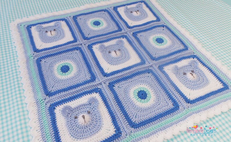 K&ouml;nnte beinhalten: Eine geh&auml;kelte Babydecke in einem blauen, wei&szlig;en und gr&uuml;nen Farbschema. Die Decke zeigt ein sich wiederholendes Muster aus B&auml;renk&ouml;pfen und Kreisen.