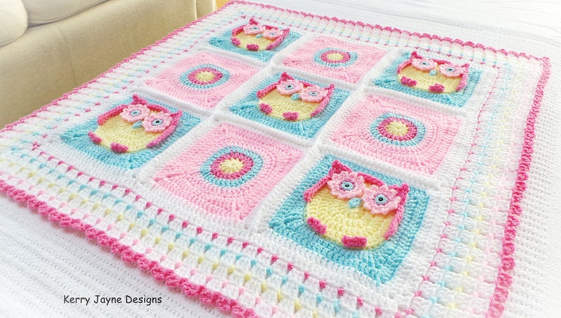 May include: A crocheted baby blanket with a pink, white, and blue color scheme. The blanket features a repeating pattern of owls and circles. The blanket is edged with a pink crocheted border. "Kerry Jayne Designs" is written in the bottom left corner.