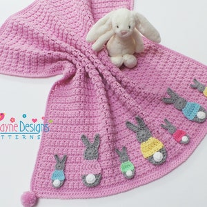 May include: A pink crocheted baby blanket with a white bunny and several colorful bunny appliques. The blanket has a pom-pom on each corner.