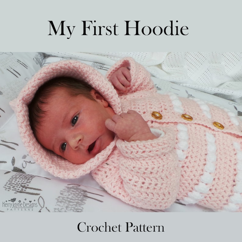 May include: A pink crocheted baby hoodie with white accents and buttons. The hoodie has a hood and is designed for a newborn baby. The text "My First Hoodie" and "Crochet Pattern" are visible in the image.
