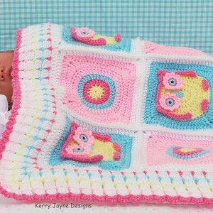 May include: A pink, blue, and white crocheted baby blanket with a border of pink and white. The blanket features a repeating pattern of owls and circles. The blanket is folded over a baby doll.