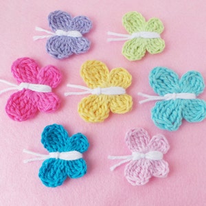 May include: Seven crocheted butterflies in different colors, including purple, pink, yellow, blue, and light pink. The butterflies are arranged on a pink background.  CROCHET PATTERN is written vertically on the left side of the image.