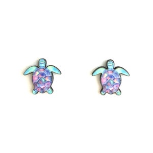 May include: A pair of stud earrings featuring a watercolor-style sea turtle design with shades of blue, purple, and pink.