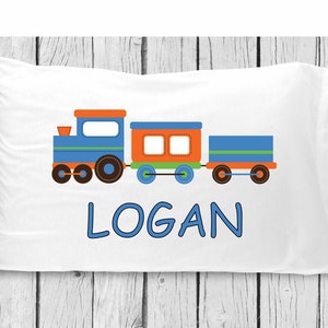 May include: A white pillowcase with a blue and orange train design and the name "LOGAN" printed in blue.