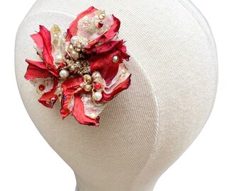 Op de afbeelding: Een rood en goudkleurig bloemen haaraccessoire met parel- en kristalaccenten. De stoffen bloem is bevestigd aan een witte hoofdvorm. Het accessoire heeft een gelaagd ontwerp met een mix van texturen en kleuren, geschikt voor speciale gelegenheden.