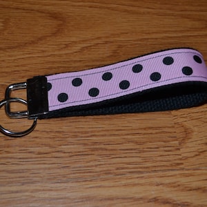 May include: A pink and black polka dot key chain with a silver double ring.