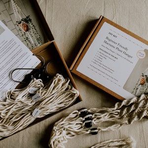 May include: A macrame plant hanger DIY kit. The box reads "Beginner Friendly Macrame Plant Hanger". The kit includes cotton cord, a brass ring, beads, and instructions. Designed for a 10-12cm pot.