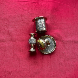 Może przedstawiać: Trzy małe, ozdobne, srebrne metalowe pojemniki z misternymi wzorami. Pojemniki znajdują się na czerwonym tle z tkaniny.