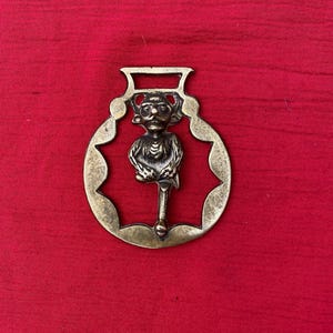 May include: A brass horse shoe charm with a detailed figure of a goblin or imp holding a staff. The charm is a traditional good luck charm.