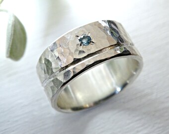 May include: A silver hammered band ring with a small blue gemstone set in the center.