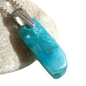 May include: A turquoise blue gemstone pendant on a silver chain. The pendant is a long, rectangular shape with a smooth, polished surface. The chain is a delicate, silver chain with a lobster clasp.