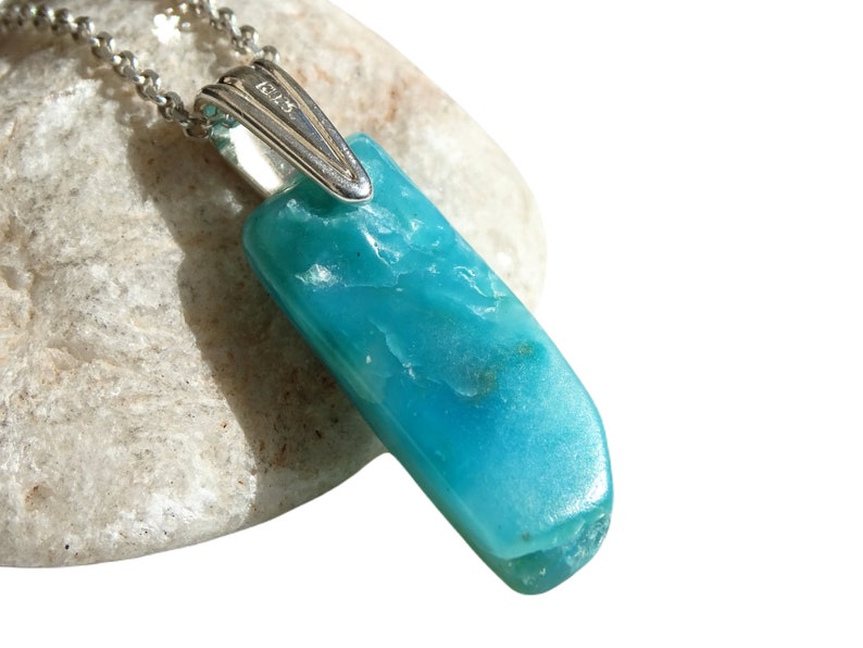 May include: A turquoise blue gemstone pendant on a silver chain. The pendant is a long, rectangular shape with a smooth, polished surface. The chain is a delicate, silver chain with a lobster clasp.
