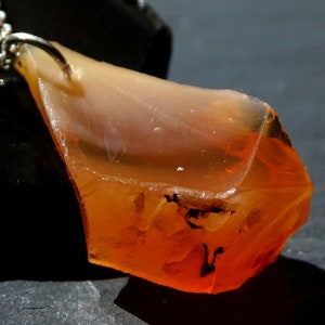 May include: A pendant necklace featuring a large, irregularly shaped orange and clear gemstone. The gemstone has a rough, natural texture and is attached to a silver chain.