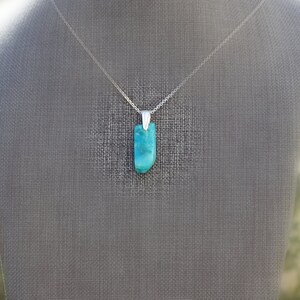May include: A silver chain necklace with a turquoise pendant. The pendant is a smooth, rectangular shape with a light blue and green color.