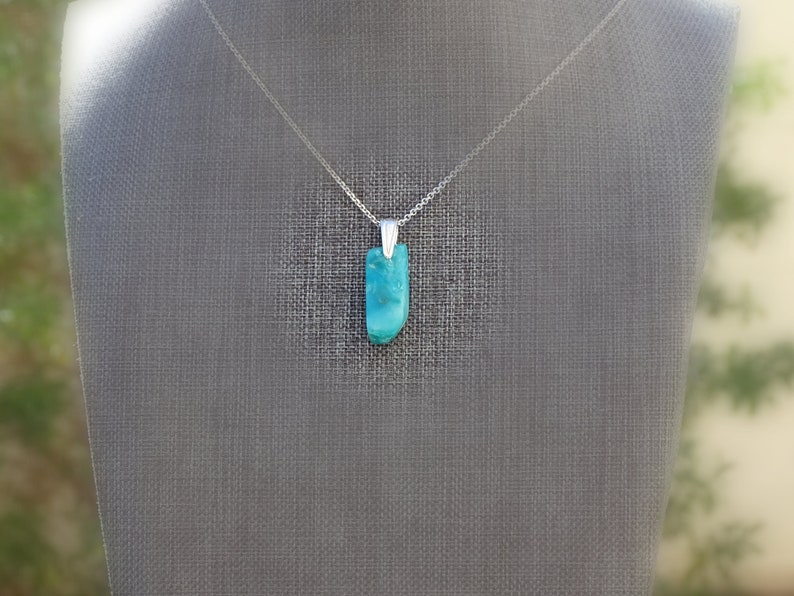 May include: A silver chain necklace with a turquoise pendant. The pendant is a smooth, rectangular shape with a light blue and green color.