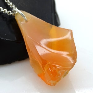 May include: A pendant necklace featuring a large, orange, raw opal stone. The opal is set in a silver bail and hangs from a silver chain.